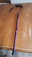 Full view of the lightweight metal cane with colorful patterned shaft on wooden table.