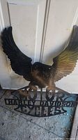 Photo showing upper portion of black metal eagle with outstretched wings and some rust patina on the metal surface.