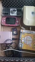 Mixed lot items including two Nintendo Gameboy Advance consoles, Nintendo DS, game cartridges, DVD case with games, label maker, and cables.