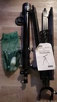Full lot showing telescope tube, tripod stand, and green mesh bag with accessories on wooden floor