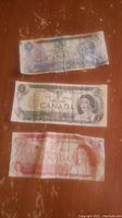 Three Canadian banknotes lying flat showing wear and tear and detail of front side.