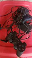 Two wired Sony PlayStation-style controllers tangled with cables, showing button details and cable connectors.
