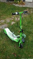 Full view of the green Razor electric scooter showing handlebar grips, front wheel, deck with foot pegs, and attached seat.