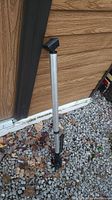 Full length view of a metal truck bed hanger standing on gravel and next to a siding wall.
