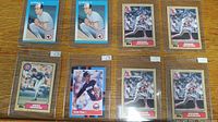 Top view of 8 baseball cards arranged on a wooden table, all in plastic card covers. Multiple cards showing Reggie Jackson and others including Greg Jorgensen and Nolan Ryan.
