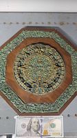 Full view of wooden Aztec calendar art with Mexican jade inlay and 100 dollar bill for size reference.