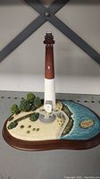Full view of the Barnegat Light miniature lighthouse with surrounding landscape and water on oval base.