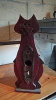 Front view of wooden birdhouse shaped like a cat with carved details and entrance hole.
