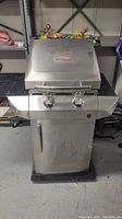 Full frontal view of stainless steel gas barbecue grill with two knobs, lower cabinet door, and side shelves.
