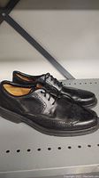 Pair of Clark's black men's dress shoes on metal shelf, showing side and top views with detailing.