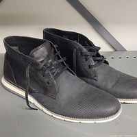 Side angle view of the pair of black textured leather lace-up men's boots with white soles
