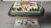 Full view of the Ellis Island miniature model with a hundred dollar bill for scale showing the base representing water and the building's roof and architectural features