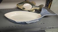 Fish-shaped ceramic serving tray and fish wall frame displayed on shelf showing overall appearance and shape.
