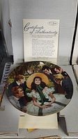 Close-up of first collectible plate featuring Scarlett O'Hara with men surrounding her, certificate of authenticity displayed behind the plate inside original box.