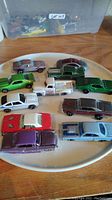 View of 11 Hot Wheels cars placed on a white plate, showcasing various colors and styles including green, purple, white, red and blue.