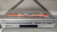 Front view of the JVC VHS DVD combo unit showing control buttons, VHS and DVD slots, and connection ports.