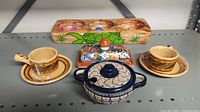 Photo of all five Mexican pottery pieces on shelf including cups, butter dish, pot, and condiment holder