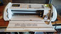 Front view of the white Provo Craft Cricut machine showing the paper slot, cutting mechanism, and open door.