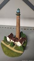 Front view of the Danbury Mint Shinnecock Lighthouse miniature showing detailed lighthouse tower and attached buildings with landscaping base.