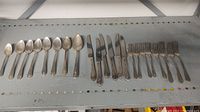 22 pieces of silverware arranged on a shelf including spoons, knives, and forks showing tarnish.
