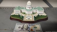 Front view of the US Capitol Building miniature with a $100 bill for scale showing detailed features and green roof.