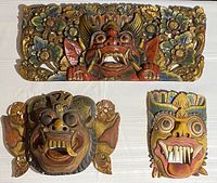 Three carved Balinese style items: two masks and a floral mythic wall plaque, all painted and wood-carved, arranged on a light surface.