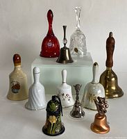Photo showing the complete collection of ten decorative bells, highlighting the variety in materials and sizes including glass, ceramic, metal, and enamel bells.