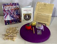 Full overview of the bobbin lace kit components including bobbins, books, pillow, pincushion, thread balls, wooden tool, and instruction sheets.