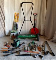 Full view of garden tools laid out with Scotts Classic push mower and red shovel in the back.