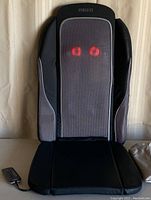 Full front view of the Homedics Shiatsu Back Massager showing the black seat pad, grey mesh back pad with black side panels, and two red glowing nodes through the mesh, with black wired remote control visible.