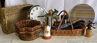 Photo showing a group of household items including 3 woven baskets, bell-shaped cast iron doorstop, IKEA clock, umbrellas, colorful glass plate, pepper mill and coffee thermos.