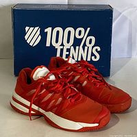 Pair of red and white K-Swiss women's tennis shoes with original blue shoe box in background labeled '100% Tennis'. Shoes show very light wear with clean uppers and laces.