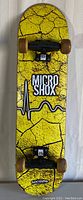 Top view of skateboard deck showing yellow cracked design and MicroShox Oxygen branding with wheels and trucks attached.