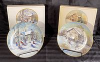 Both Keirstead collector plates with original boxes, displayed on plate stands, showing front artwork and box covers with identical winter scenes.