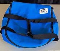 Blue Pyrex Portables insulated casserole carrier lying flat showing black straps and Pyrex logo patch on top.