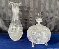 Photo shows crystal decanter and covered candy dish side by side on blue surface with black background.