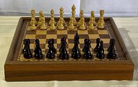 Front view of wooden chessboard with all chess pieces positioned for start of game, showing details of board and pieces.