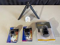 Travel adapters and tripod arranged on table: Targus World Power travel adapter in packaging, NexxTech type D and GAB adapters in packaging, and small black tripod