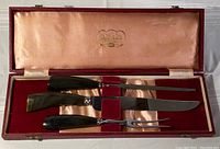 Vintage carving set in red leather box with satin and velvet interior, showing buffalo horn handles and stainless steel blades and fork arranged in box.