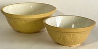 Pair of yellow stoneware mixing bowls with white interiors side by side