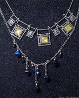Front view of two necklaces on black bust stand showing 16" GILI silver choker with square crystals and 20" silver chain with blue bead dangles.