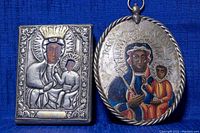 Photo shows two religious wall plaques against a blue fabric background. The left plaque is rectangular with a crowned Madonna and Child in relief. The right plaque is oval with a painted Madonna and Child and a twisted rope border.