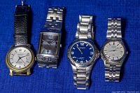 Four men's vintage wristwatches displayed side by side, two with metal straps, one leather, one metal bracelet style.