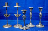 Full view of five silver-plated candleholders against blue background showing two pairs and one single holder.