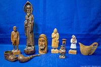 Full group of nine assorted wooden carvings against blue background, showing various religious and vintage themes