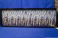 Full view of the framed Star Wars poster showing a crowd of stormtroopers in white armor against a blue background surface.