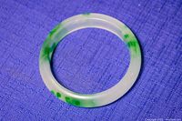 Full top view of the translucent white jade bangle with green veining, displayed on a purple textured fabric.