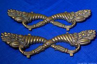 Pair of old bronze furniture accents placed on blue fabric background, showing front angle view