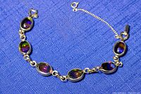 Full view of vintage bracelet laid flat showing gold plated links and multicolor oval rhinestones along with safety chain.