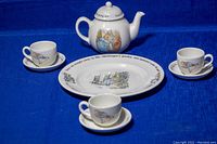 Full set arrangement of teapot, 8-inch plate, and three teacups with saucers on blue background, showing all items together.